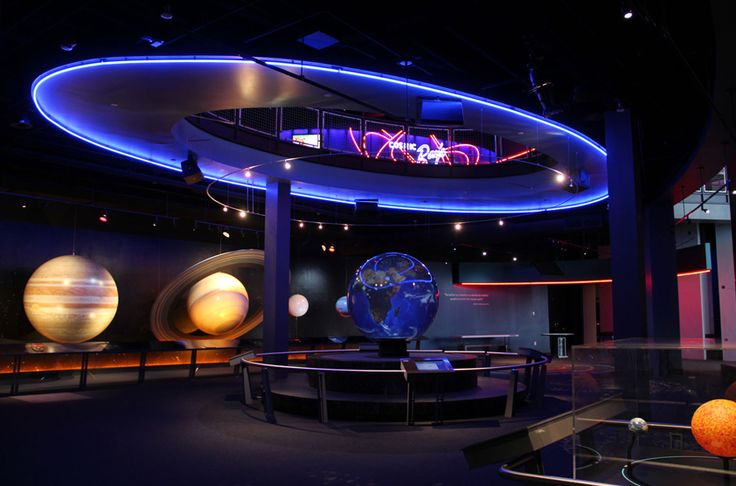 an image of a museum setting with planets in the center and lights on display behind it