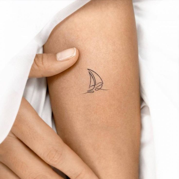 a woman's arm with a small sailboat tattoo on the back of it