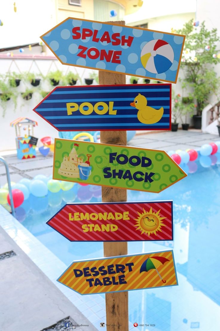 a wooden pole with signs on it in front of a swimming pool