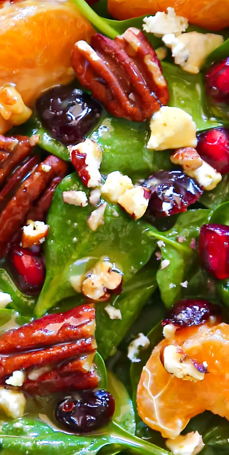 a salad with oranges, cranberries and pecans is shown close up