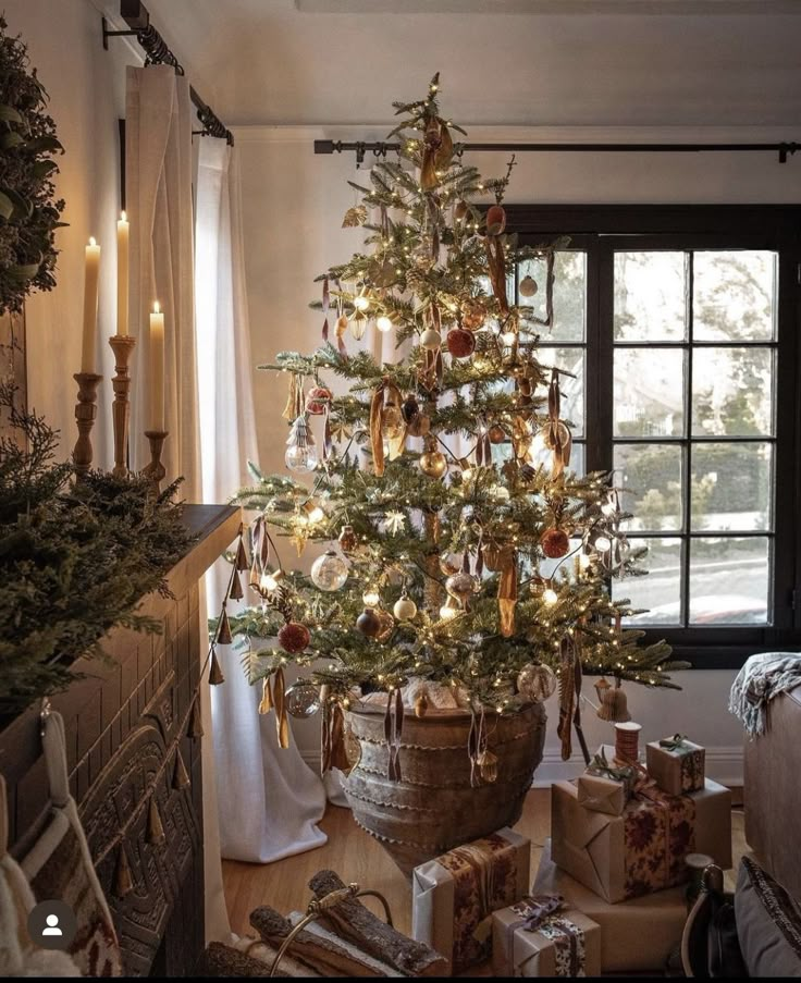 a decorated christmas tree in a living room next to a window with candles and presents