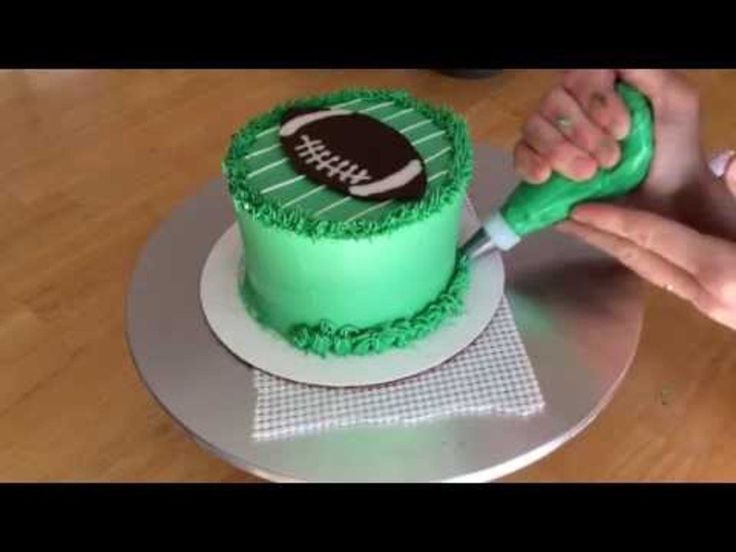 someone is decorating a cake with green frosting and a football on the top