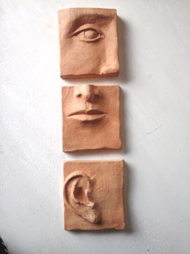 three clay faces are shown on a white surface