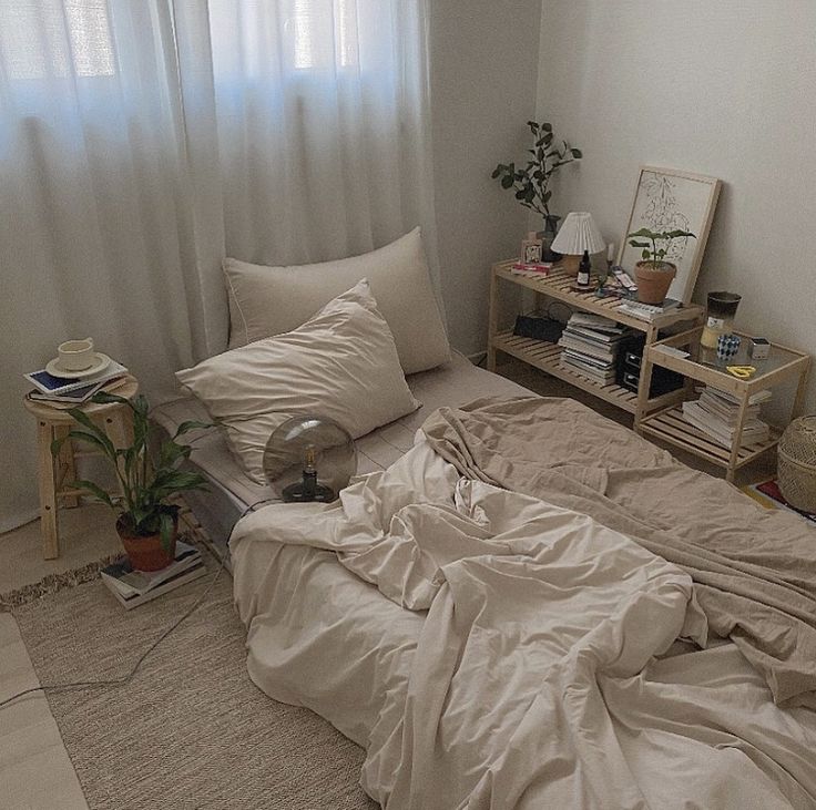 an unmade bed with white sheets and pillows in a room next to a window