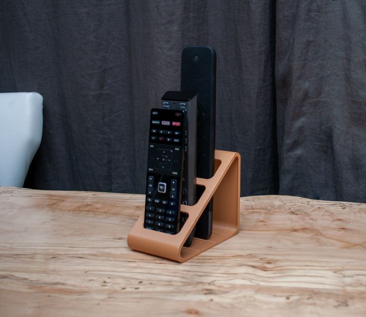 a cell phone and remote control sitting on a wooden table with a black curtain in the background