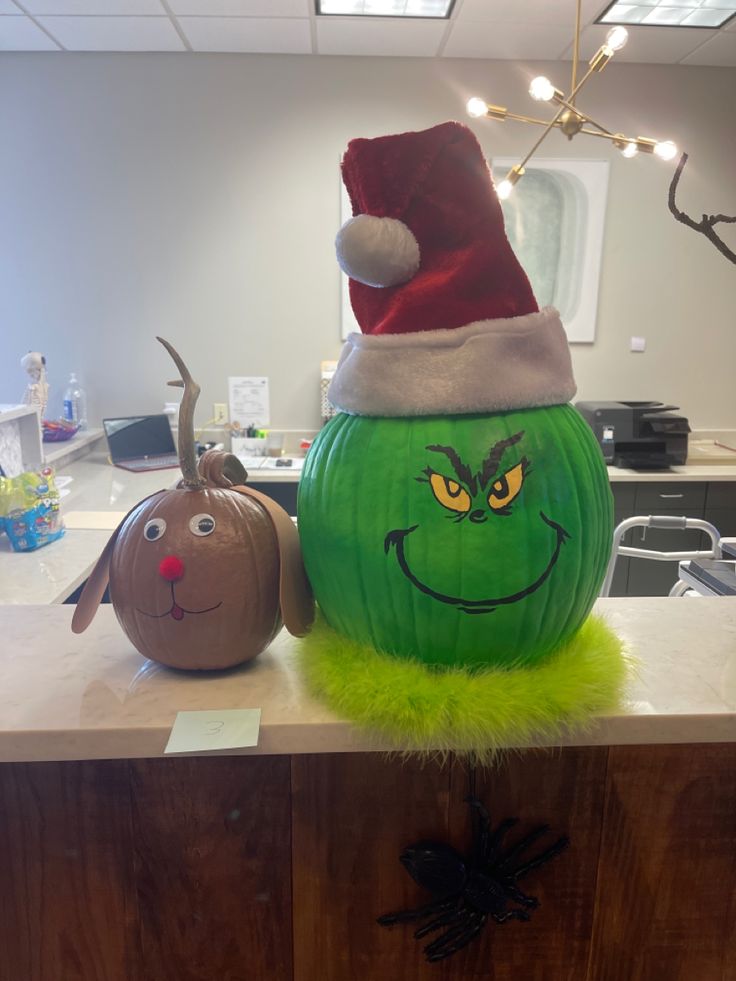 a green pumpkin with a grin face painted on it and a santa hat sitting on top