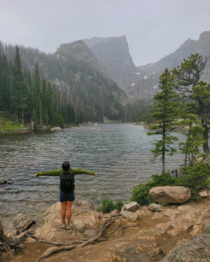 a person standing on the edge of a lake with their arms spread out in front of them