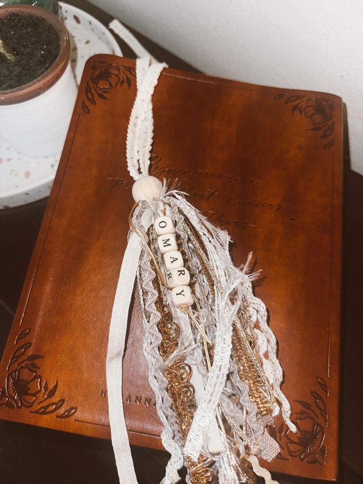 a brown book with white ribbon on it sitting on a table next to a potted plant