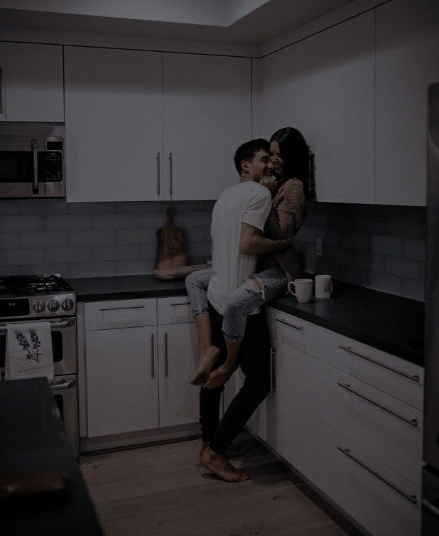 a man and woman hug in the kitchen while they stand on the counter next to each other