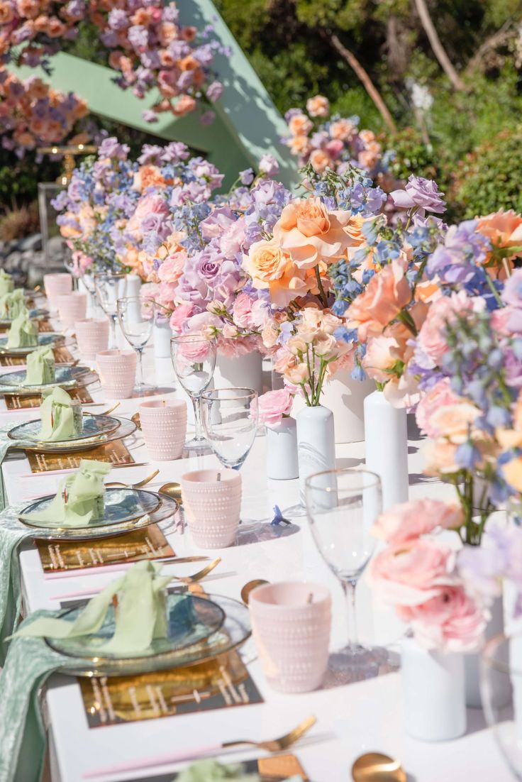 a long table is set with pink and blue flowers in vases, plates and utensils