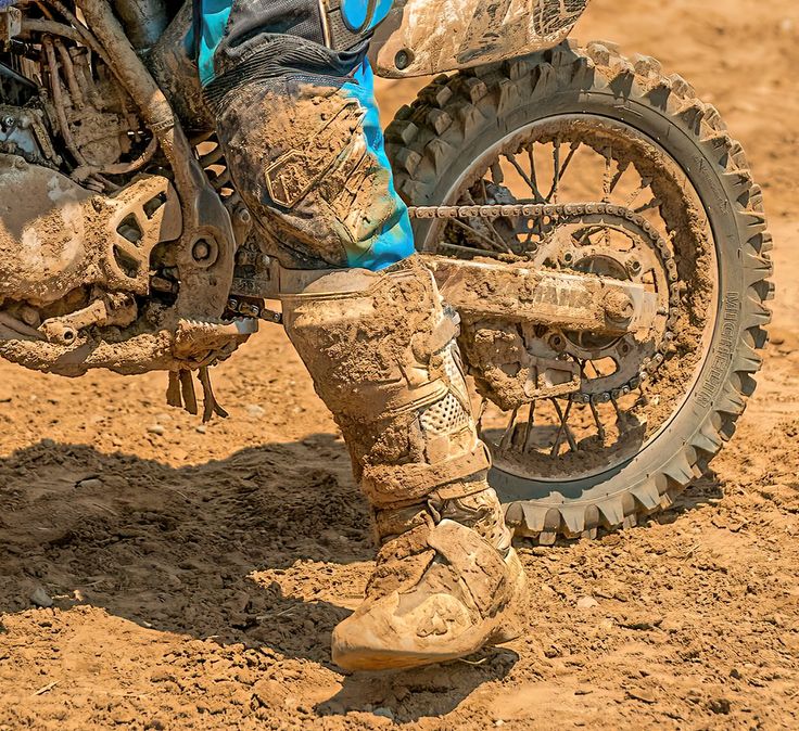 a dirt bike rider is standing on his muddy motorcycle tire and wearing blue pants with black boots