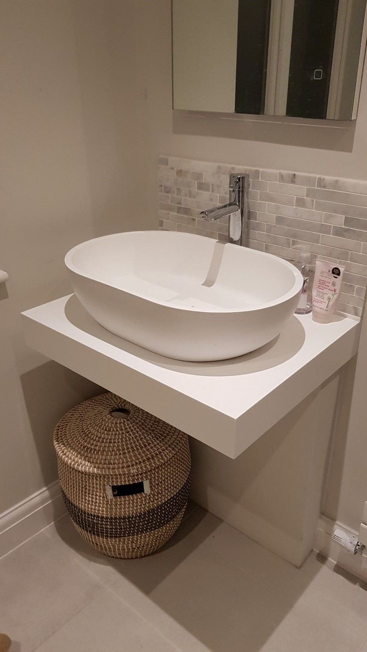 a white sink sitting under a bathroom mirror next to a basket on top of a counter