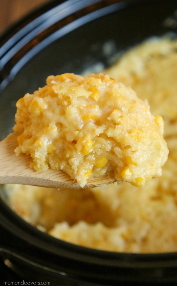 a spoon full of food sitting in a crock pot with corn on the cob