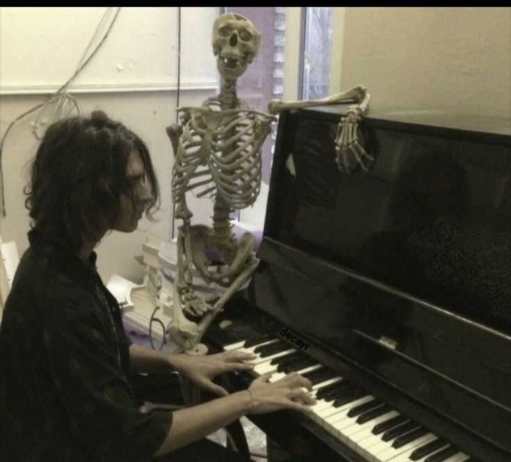 a man sitting in front of a piano with a skeleton on it