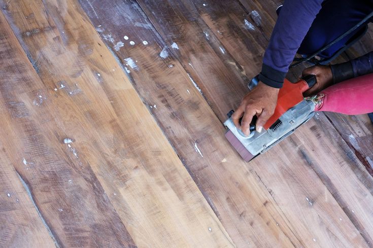 a person using a sanding machine on a wooden floor that has been stained red