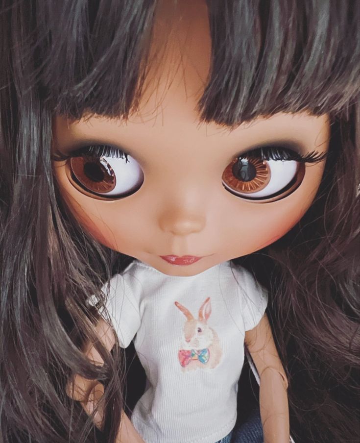 a close up of a doll with long hair and brown eyes wearing a white t - shirt