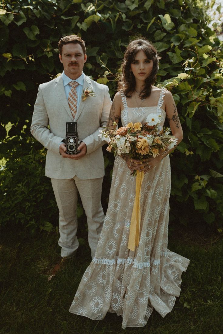 a man and woman standing next to each other in front of some bushes holding flowers