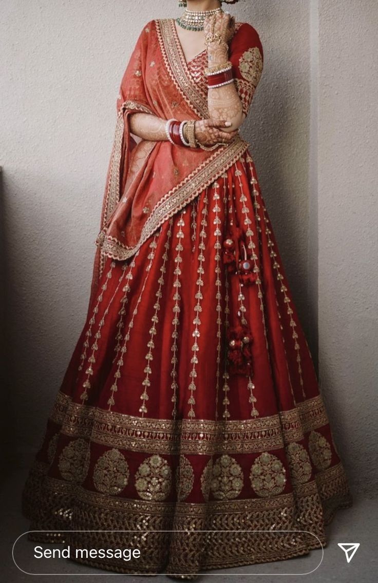 a woman in a red and gold lehenga standing next to a white wall