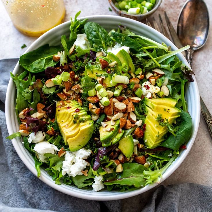 a salad with avocado, feta cheese and nuts in a white bowl