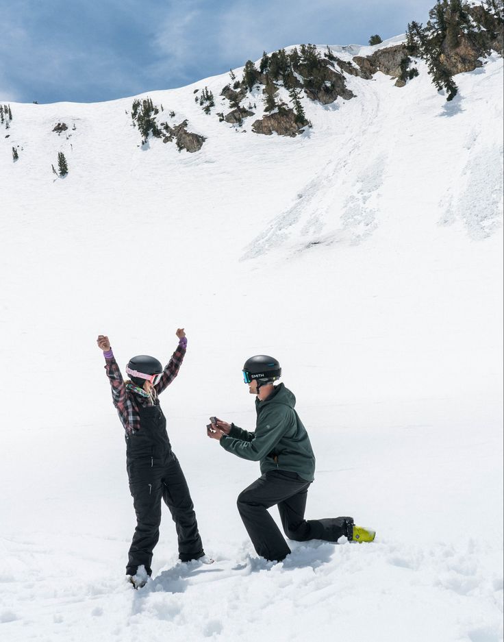 two snowboarders standing in the snow with their arms up and one holding his hands up