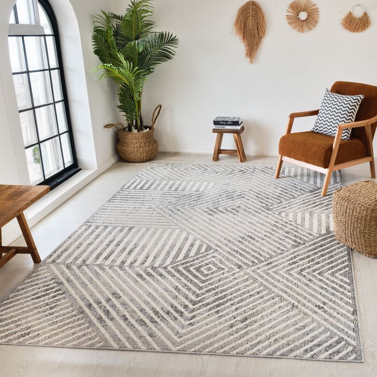 a living room with white walls and wooden chairs, rugs and potted plants