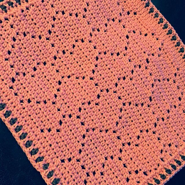 an orange crocheted blanket sitting on top of a black table next to a cup