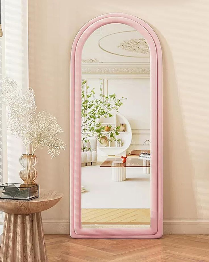 a large pink mirror sitting on top of a wooden table next to a vase filled with flowers