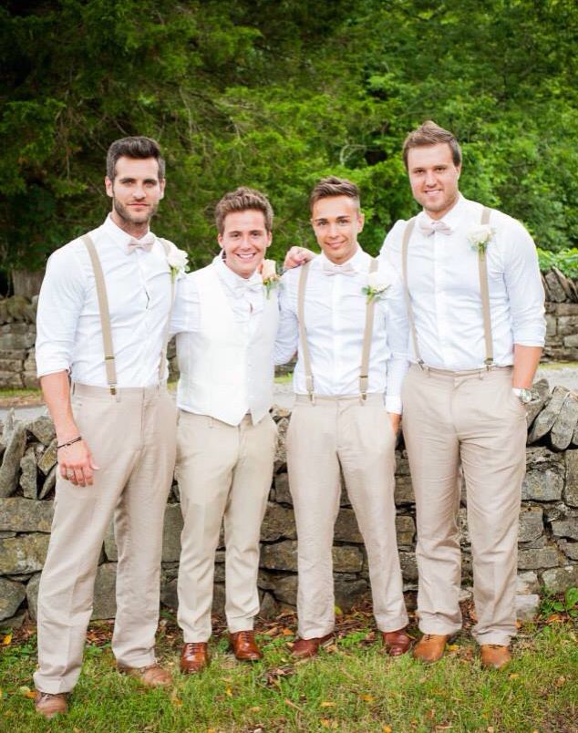 a group of men standing next to each other in front of a stone wall and trees