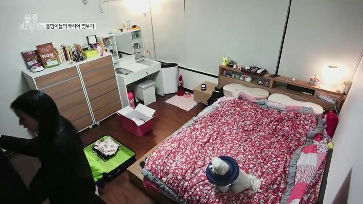 a woman standing in front of a bedroom with a bed, dresser and computer desk