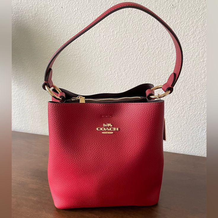 This Stunning Red/ Oxblood Colored Coach Purse Is Made Of Pebbled Leather And Features A Center Zip Compartment, A Small Interior Pocket, And A Snap Closure On Top. The Top Handle Has A 6 3/4” Drop And A Detachable Strap With A 22” Drop For Shoulder Or Crossbody Wear. Dimensions (Approx.): - 8.5” L - 8.5” H - 4” W Designer Red Rectangular Bucket Bag, Red Crossbody Bucket Bag With Gold-tone Hardware, Red Top Handle Bucket Bag With Gold-tone Hardware, Red Shoulder Bucket Bag With Gold-tone Hardware, Red Luxury Bucket Bag With Detachable Handle, Luxury Red Bucket Bag With Detachable Handle, Luxury Red Bucket Bag With Detachable Strap, Luxury Red Top Handle Bucket Bag, Elegant Red Bucket Bag