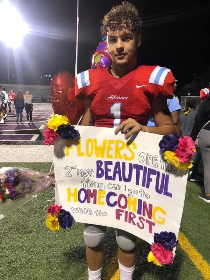 a football player holding a sign that says flowers beautiful homecoing first on the sideline