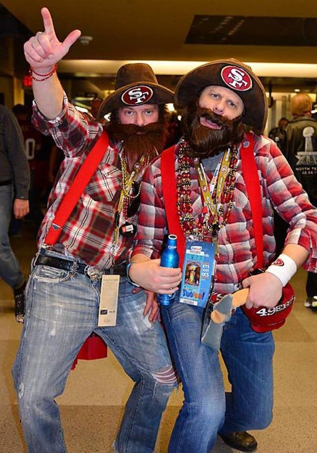 two men dressed up in costumes at an airport with one pointing to the camera and the other holding his hand up