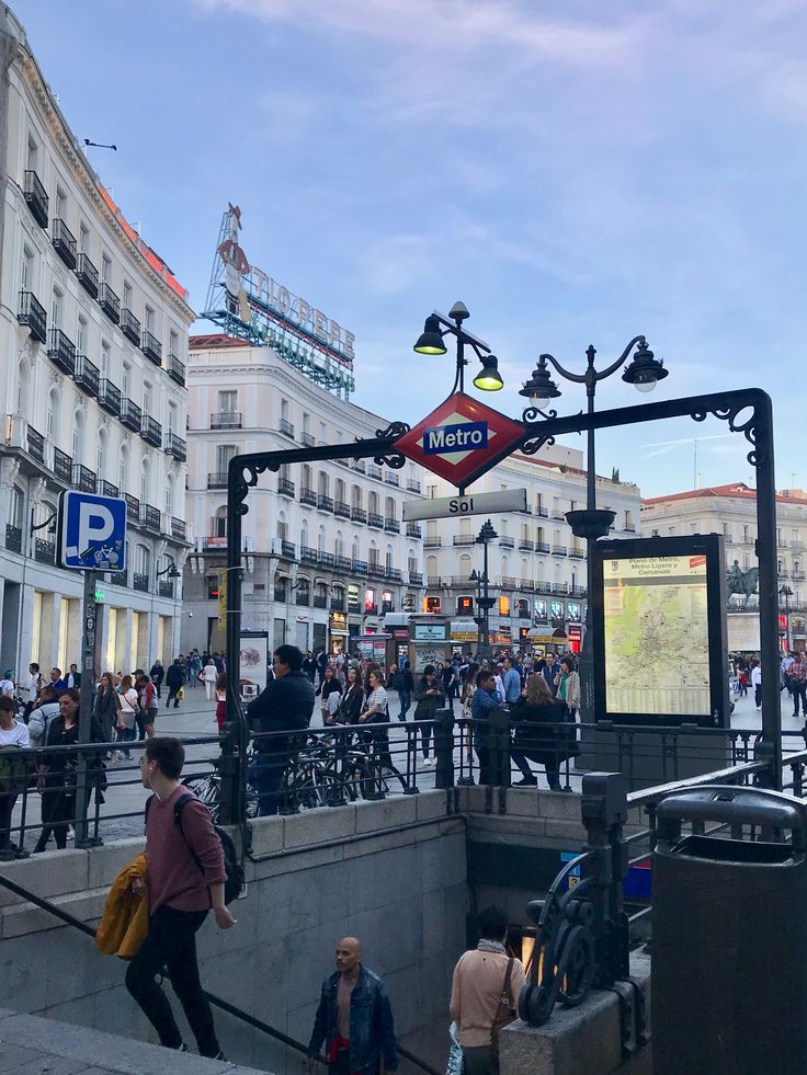 many people are walking on the street near some buildings and stairs with signs above them