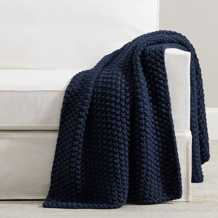 a blue crocheted blanket sitting on top of a white couch next to a white pillow