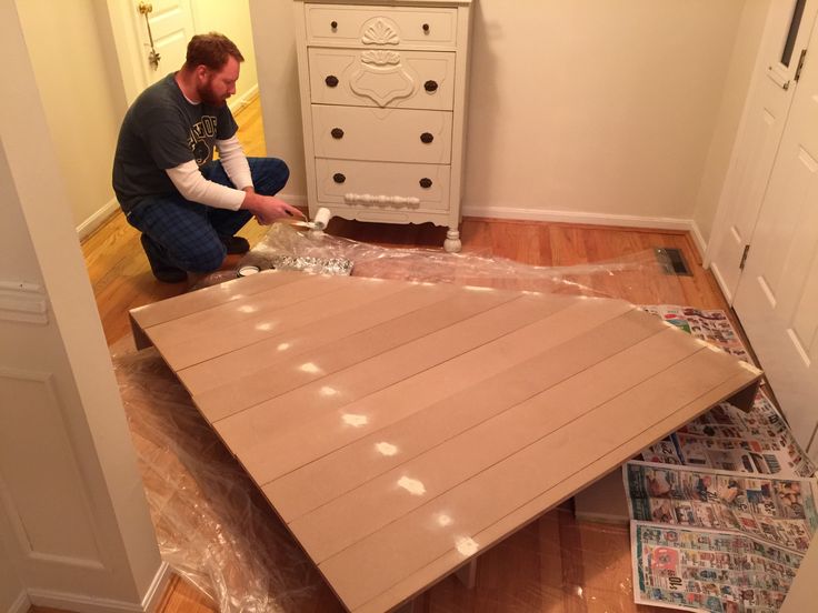 a man kneeling down on the floor next to a table that has been made out of plywood