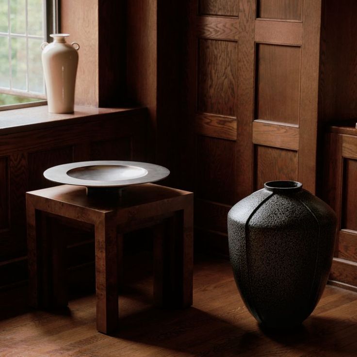 a black vase sitting on top of a wooden floor next to a table and chair