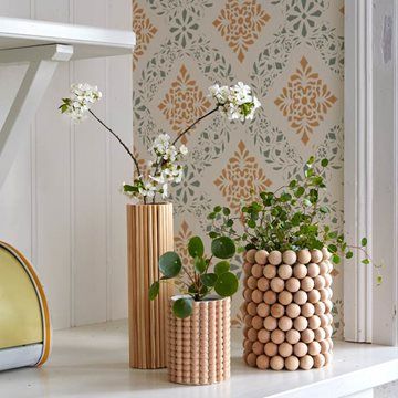 three vases with flowers and plants on a white shelf in front of a wallpapered wall