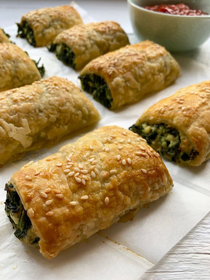 rolls with spinach, cheese and other toppings sit on a white surface next to a bowl of dipping sauce