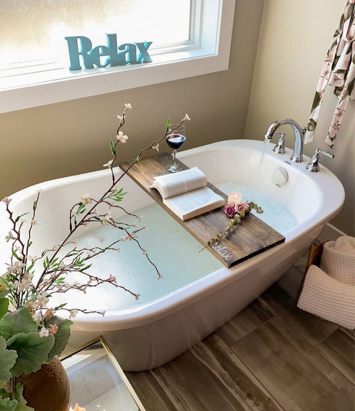 a bath tub sitting next to a window filled with flowers and books on top of it