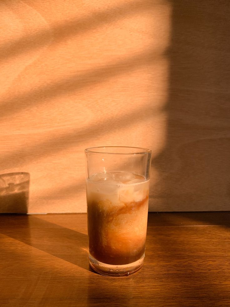 a glass filled with liquid sitting on top of a wooden table next to a cup