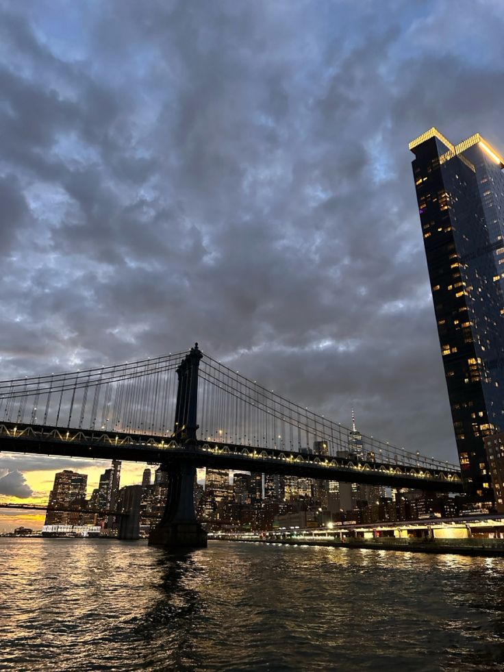 the city skyline is lit up at night as seen from across the water with a bridge in the foreground