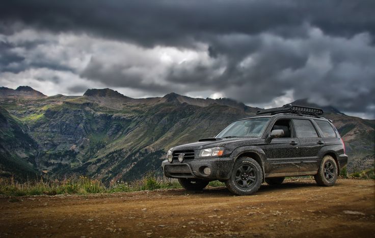 an suv parked on the side of a dirt road with mountains in the back ground