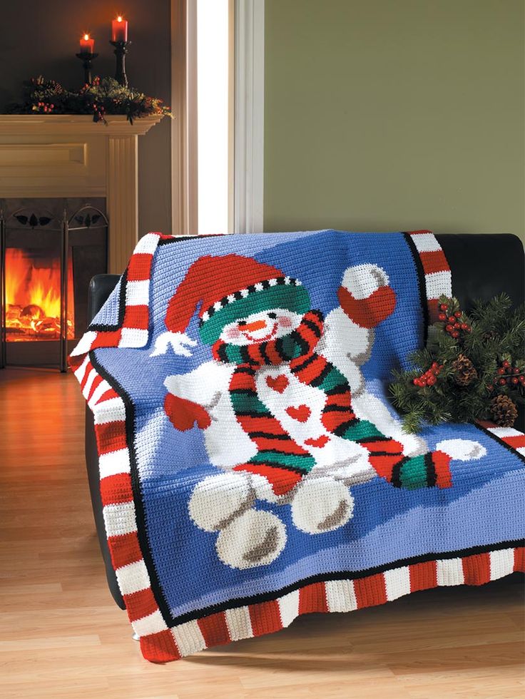 a knitted christmas blanket sitting on top of a couch next to a fire place