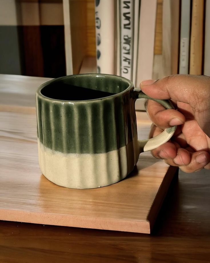 a person is holding a spoon in front of a coffee cup on a wooden table