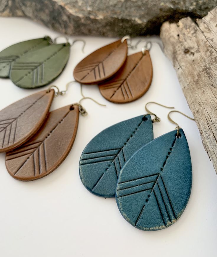 four different colored leather earrings hanging on a piece of driftwood next to a rock