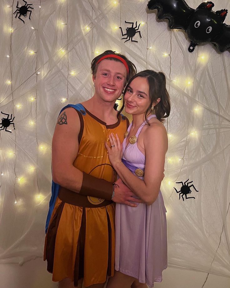 a man and woman dressed up in costumes posing for a photo with halloween decorations on the wall behind them