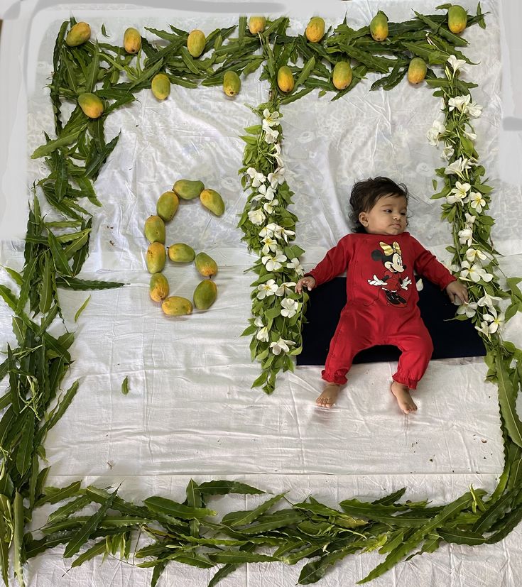 a young boy laying on top of a bed surrounded by flowers and fruit garlands