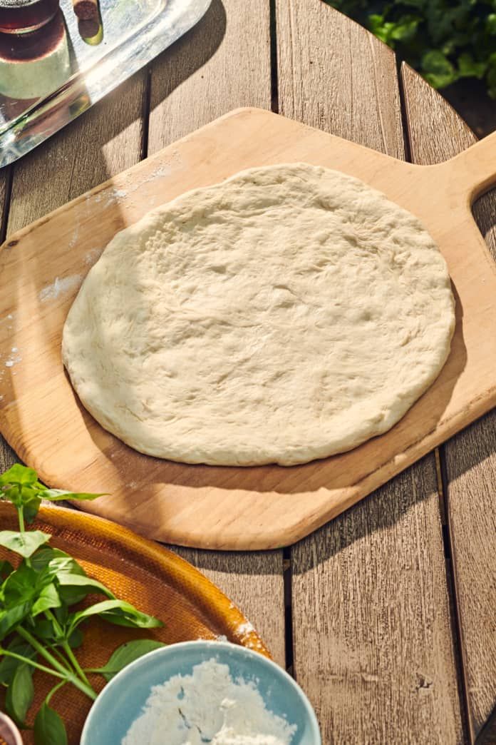 a pizza dough sitting on top of a wooden cutting board next to a blue bowl