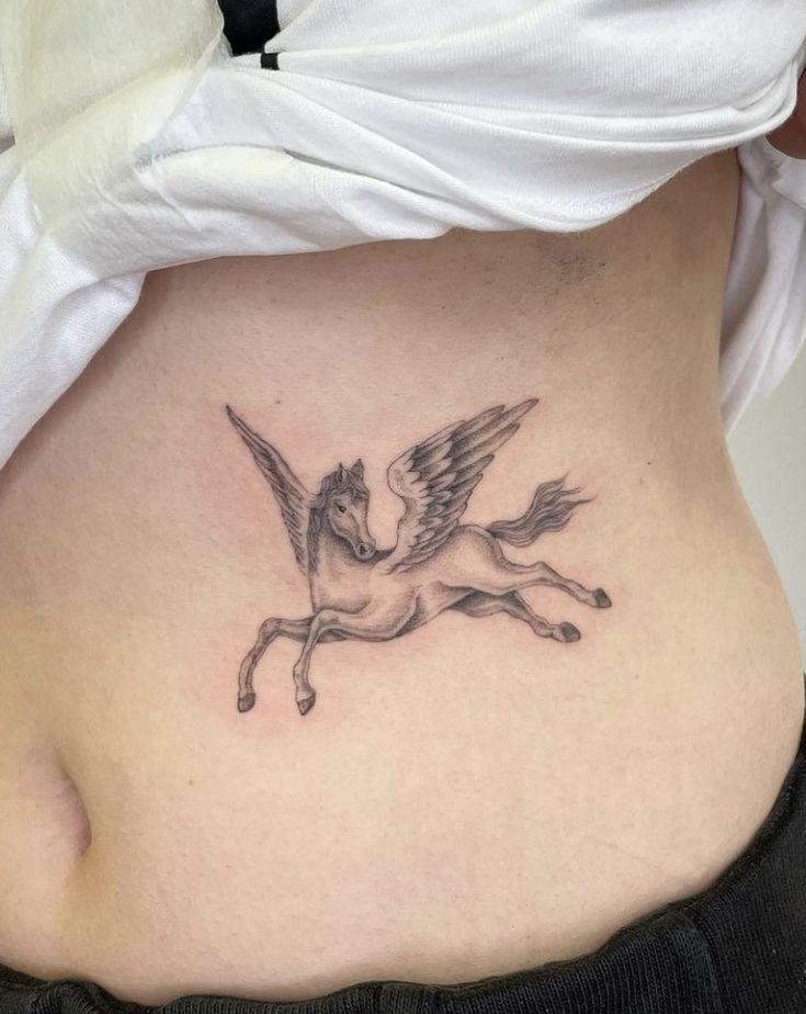 a woman's stomach with a small tattoo of a unicorn on the side and wings