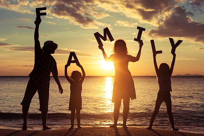 silhouettes of people holding up letters on the beach at sunset with the sun setting in the background